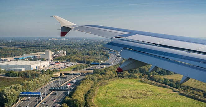A image of an aeroplane wing taken from inside the plane as it takes off from Heathrow Airport with industrial properties in the background
