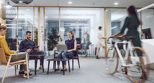 a worker walks a bike through a commercial office lobby where a group of real estate professionals are working