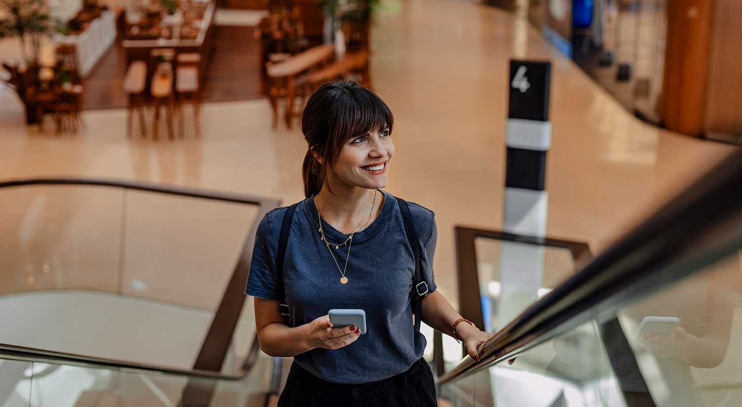 woman holding a phone rides up an escalator in a town center