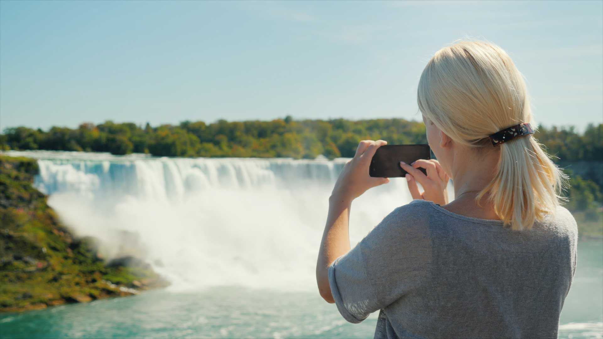 Une femme photographie une cascade avec son smartphone