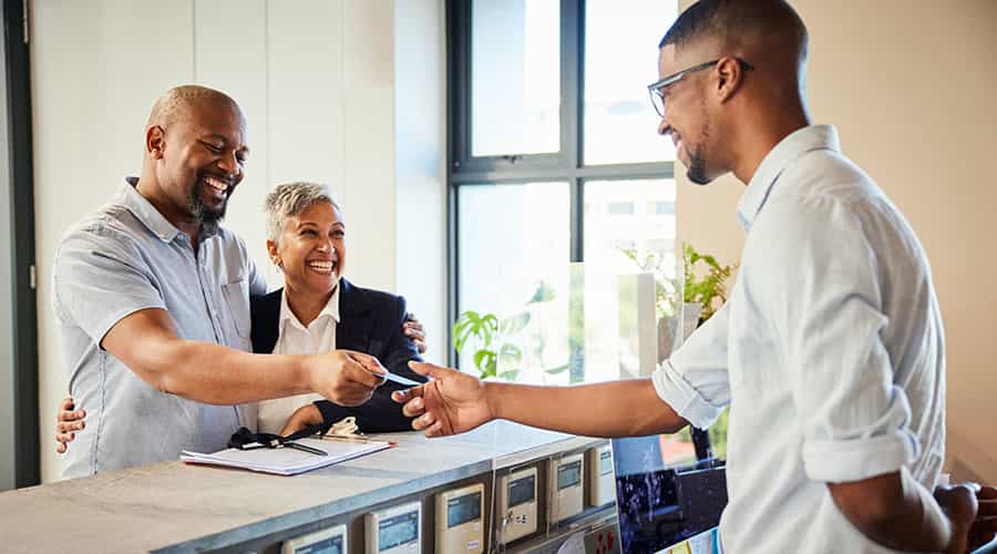 a couple checks into a Canada hotel, handing their payment card to a concierge behind a desk