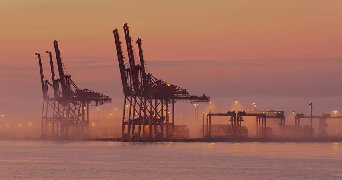 Sun setting on a port with cargo ships, cranes and containers