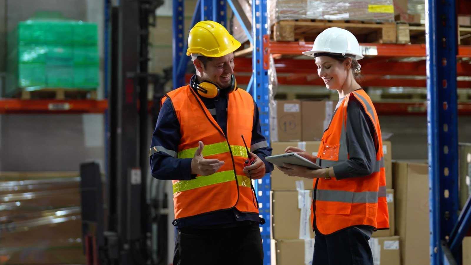 two workers wearing hard hats and high vis vests in an industrial warehouse