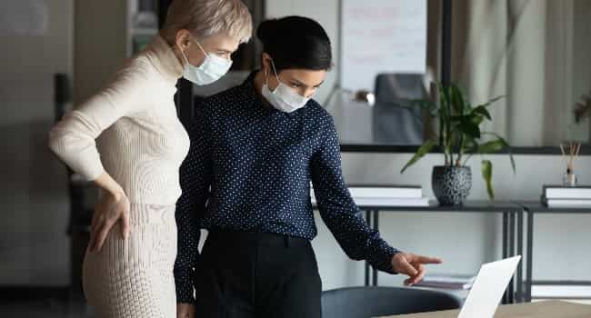 a real estate advisor discusses a lease agreement with a coleague, both wearing surgical masks