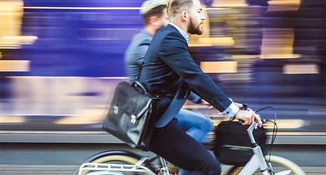 two real estate colleagues ride bicycles down the sidewalk of a busy urban environment