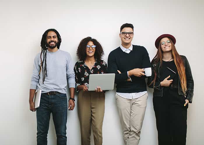 An image of four young professionals standing in front of a wall smiling to the camera