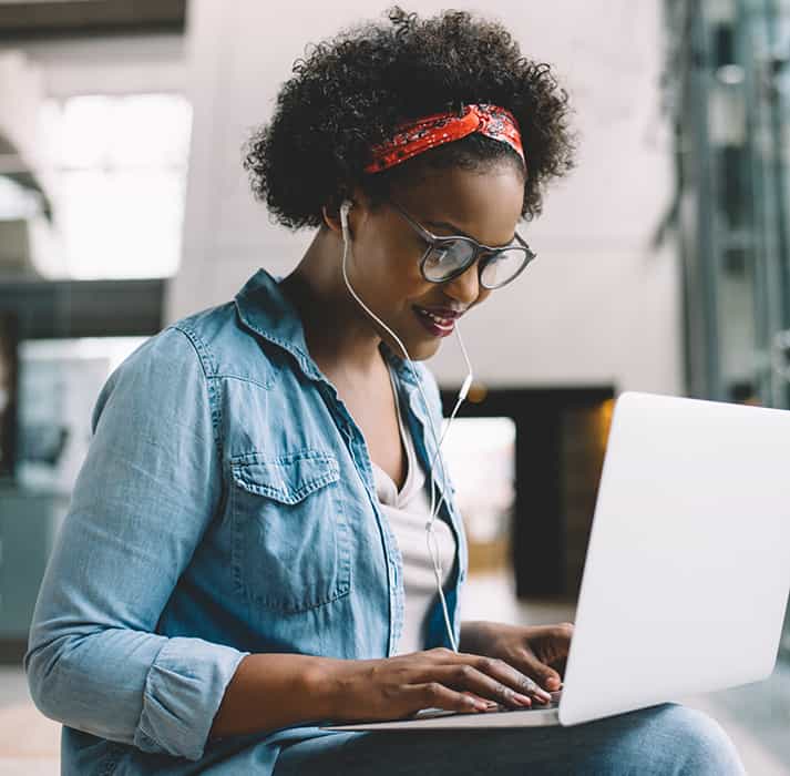 An image of a young woman wearing headphones, whilst looking at her laptop
