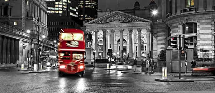 Red bus driving past the Bank of England at night
