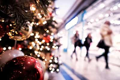 Image of a Christmas tree in the foreground with shoppers walking behind past shops