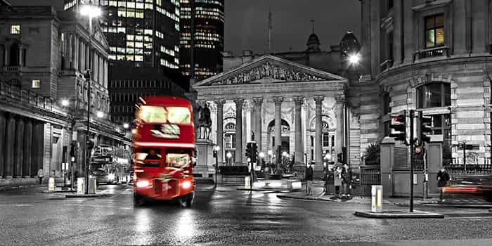 Red bus driving pass a grey image of the Bank of England in Central London