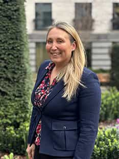 Joanna De La Porte standing outside against some flowers