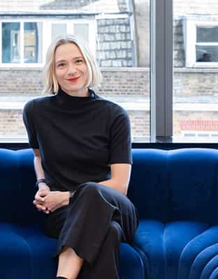 A portrait image of Kat Hanna sitting on a blue sofa