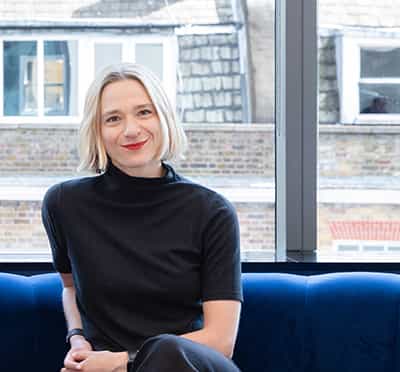 A portrait image of Kat Hanna sitting on a blue sofa