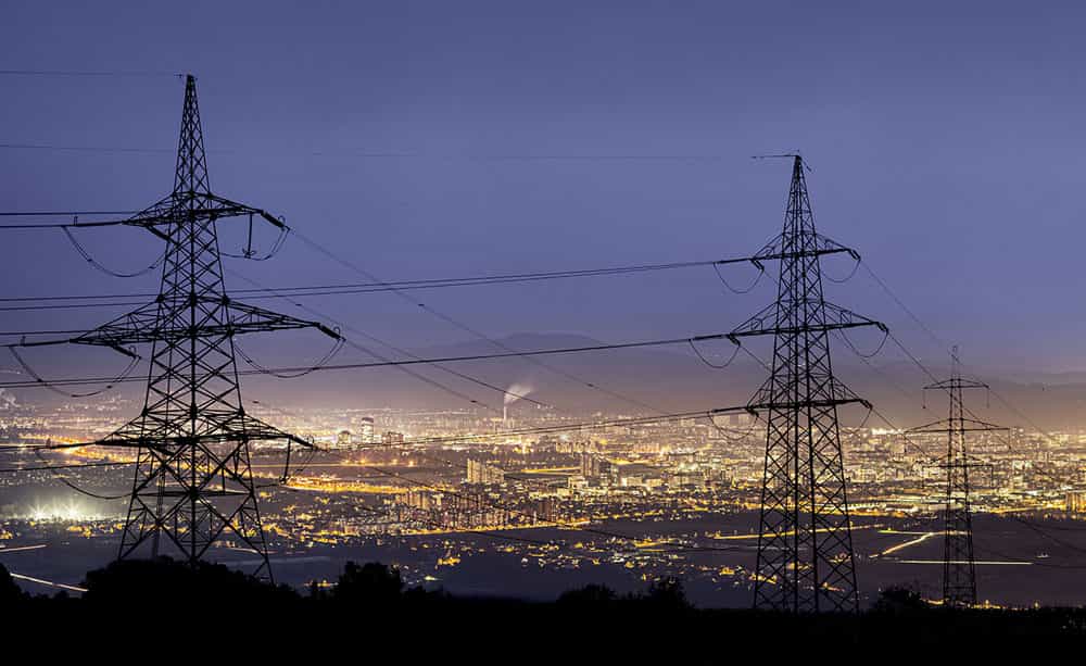 An image of a row of pylons shot above a cityscape at night