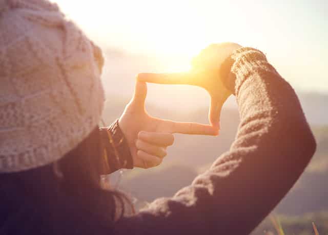 An abstract image of a woman holding up her fingers framing a scene in the distance
